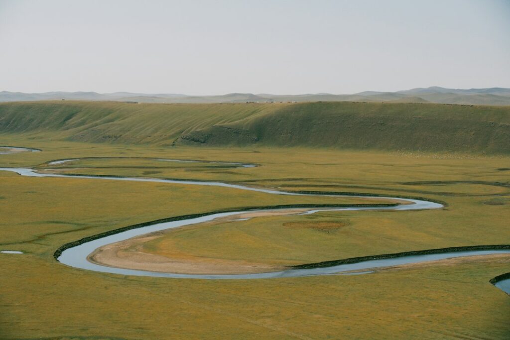 A winding river flowing through a wide grassy floodplain