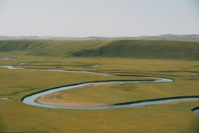 A winding river flowing through a wide grassy floodplain